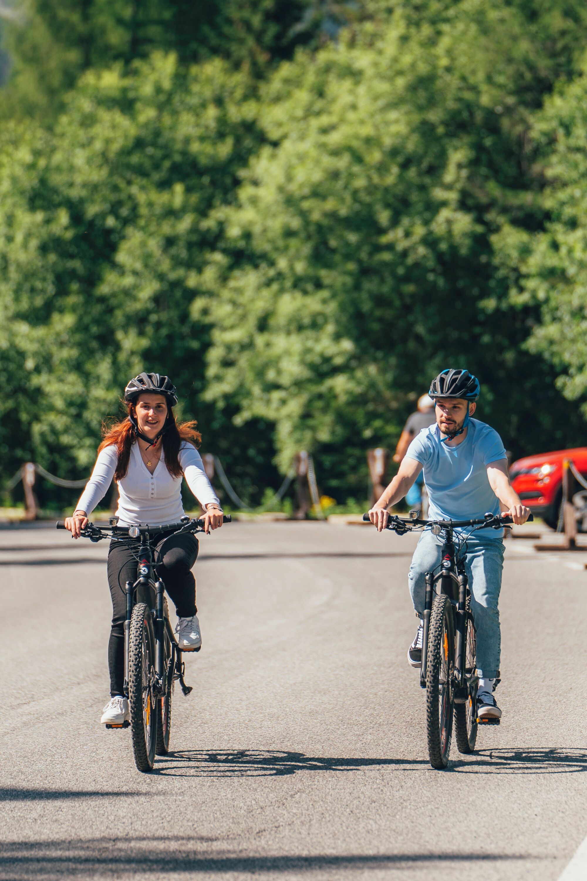 Deux personnes font du vélo sur une route, avec des arbres en arrière-plan.
