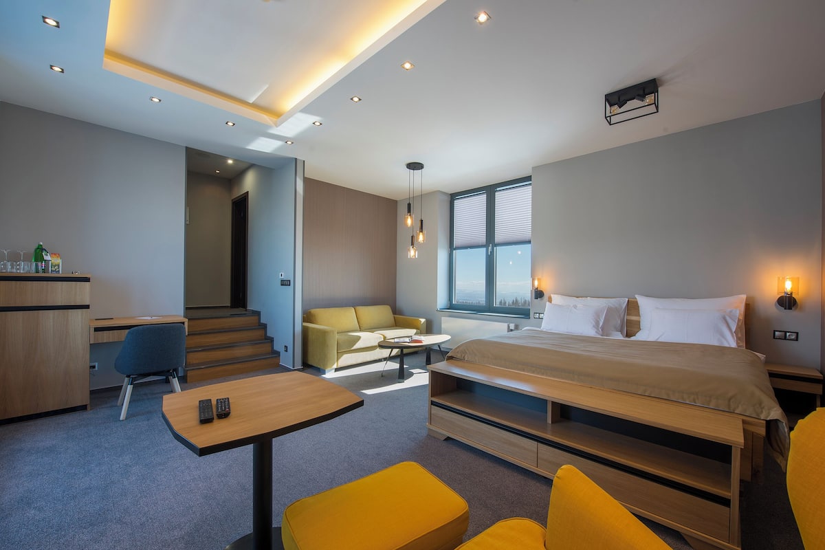A modern hotel room with a bed, a desk, a sofa, and a dining table.