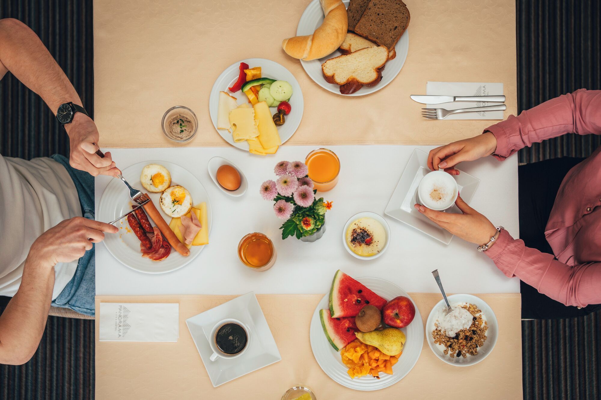 Mesa de café da manhã com diversos pratos, incluindo ovos, salsichas, torradas e frutas.