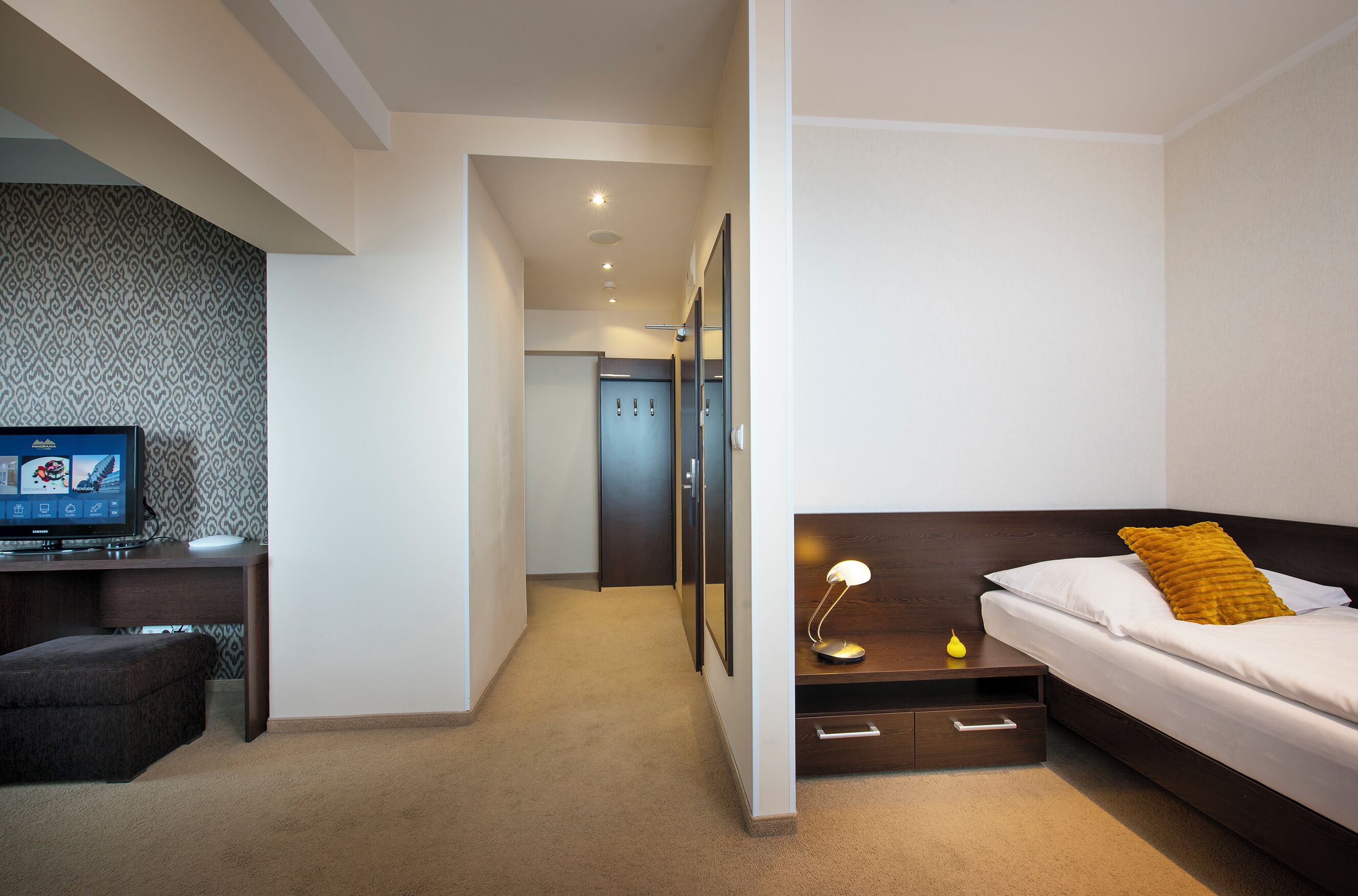 A modern hotel room with a bed, bedside table, lamp, and a television on a desk.