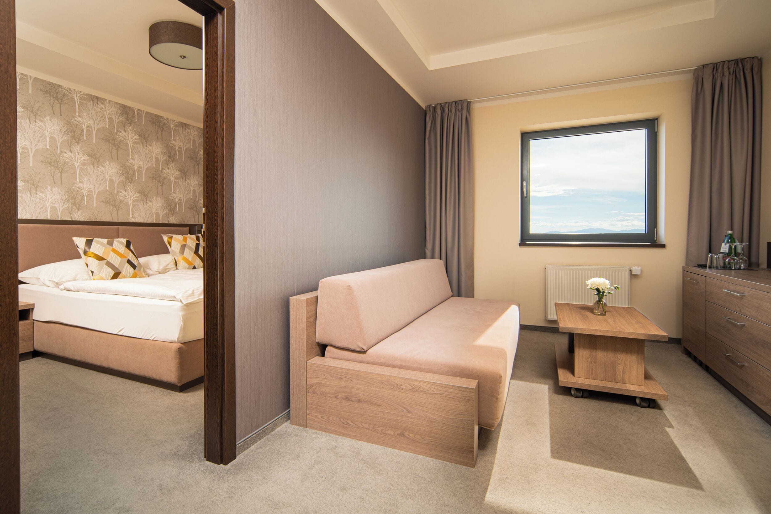 Een moderne hotelkamer met een bed, een slaapbank, een klein houten tafeltje en een raam met uitzicht.