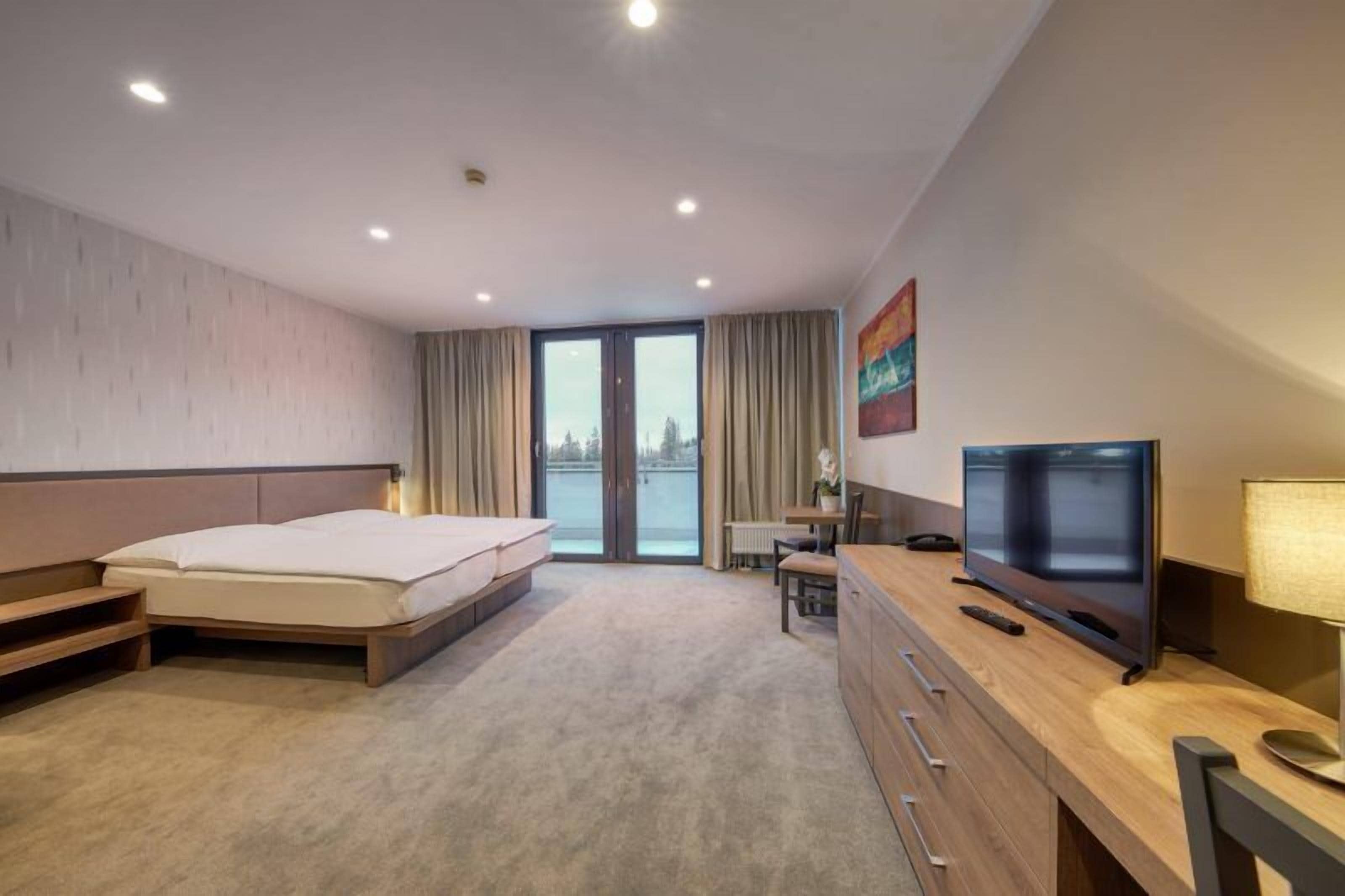 Habitación de hotel con cama, escritorio, televisor y vistas al exterior.