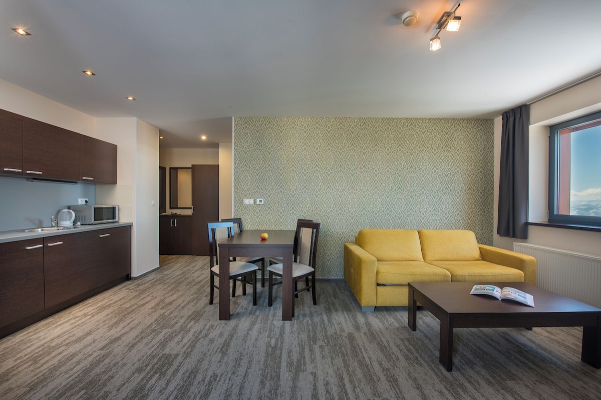 A modern living space with a dining area, a yellow sofa, and a kitchen with dark wooden cabinets.