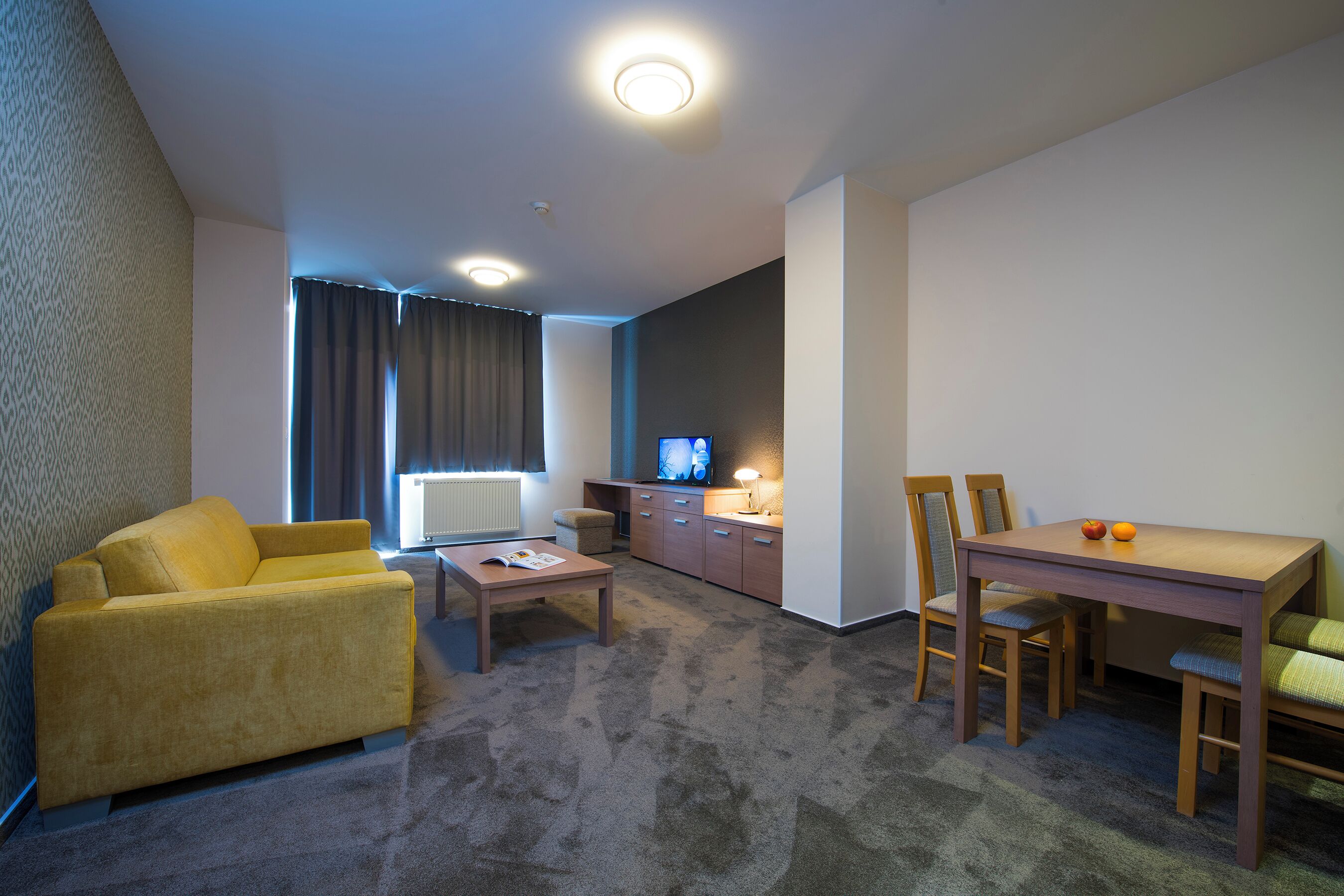 Uma sala de estar moderna com sofá, mesa de centro, televisão, mesa de jantar com cadeiras e área de cozinha.