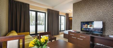 A modern hotel room with a dining area, a TV, and a large window with curtains.