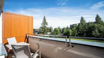 A balcony with a view of trees and buildings, a wooden panel, and a table with chairs.