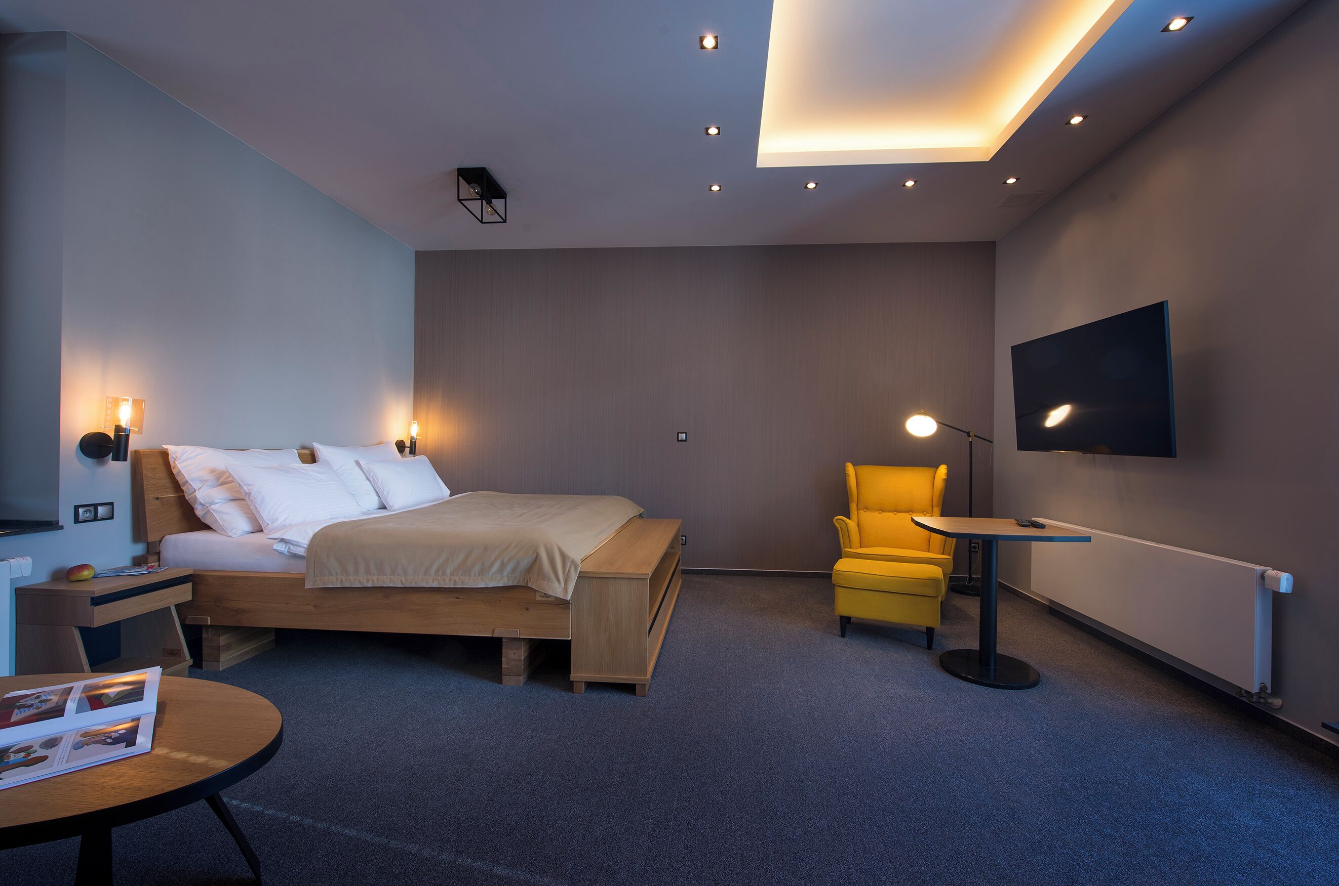 Una habitación de hotel moderna con cama, mesita de noche, lámpara, silla y televisor montado en la pared.