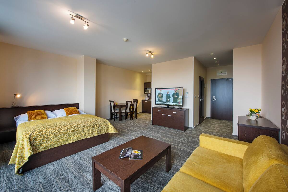 A hotel room with a bed, a sofa, a coffee table, a TV, a desk, and a chair.