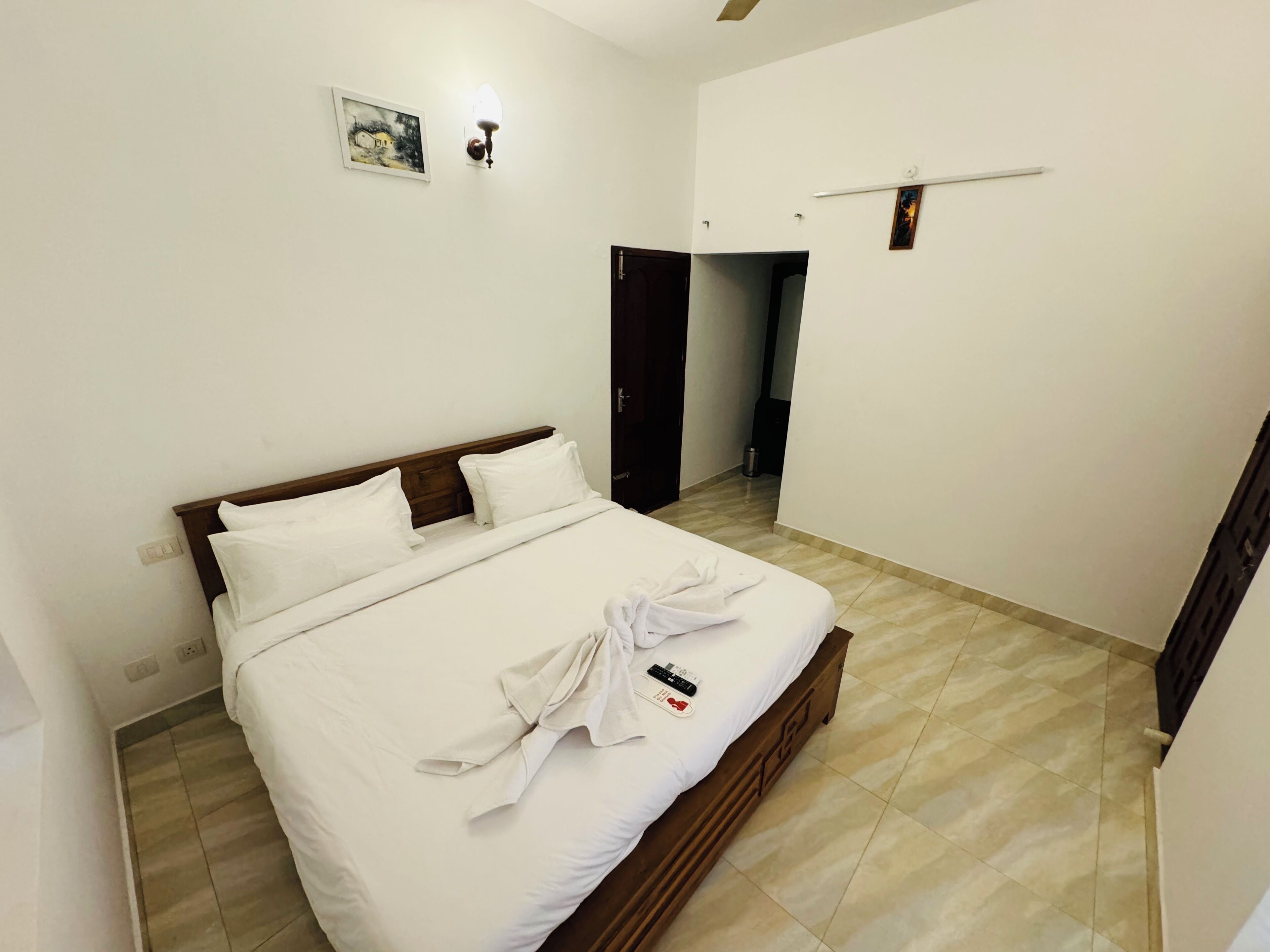 A neatly made bed with white linens and a towel, a wooden headboard, and a small painting on the wall.