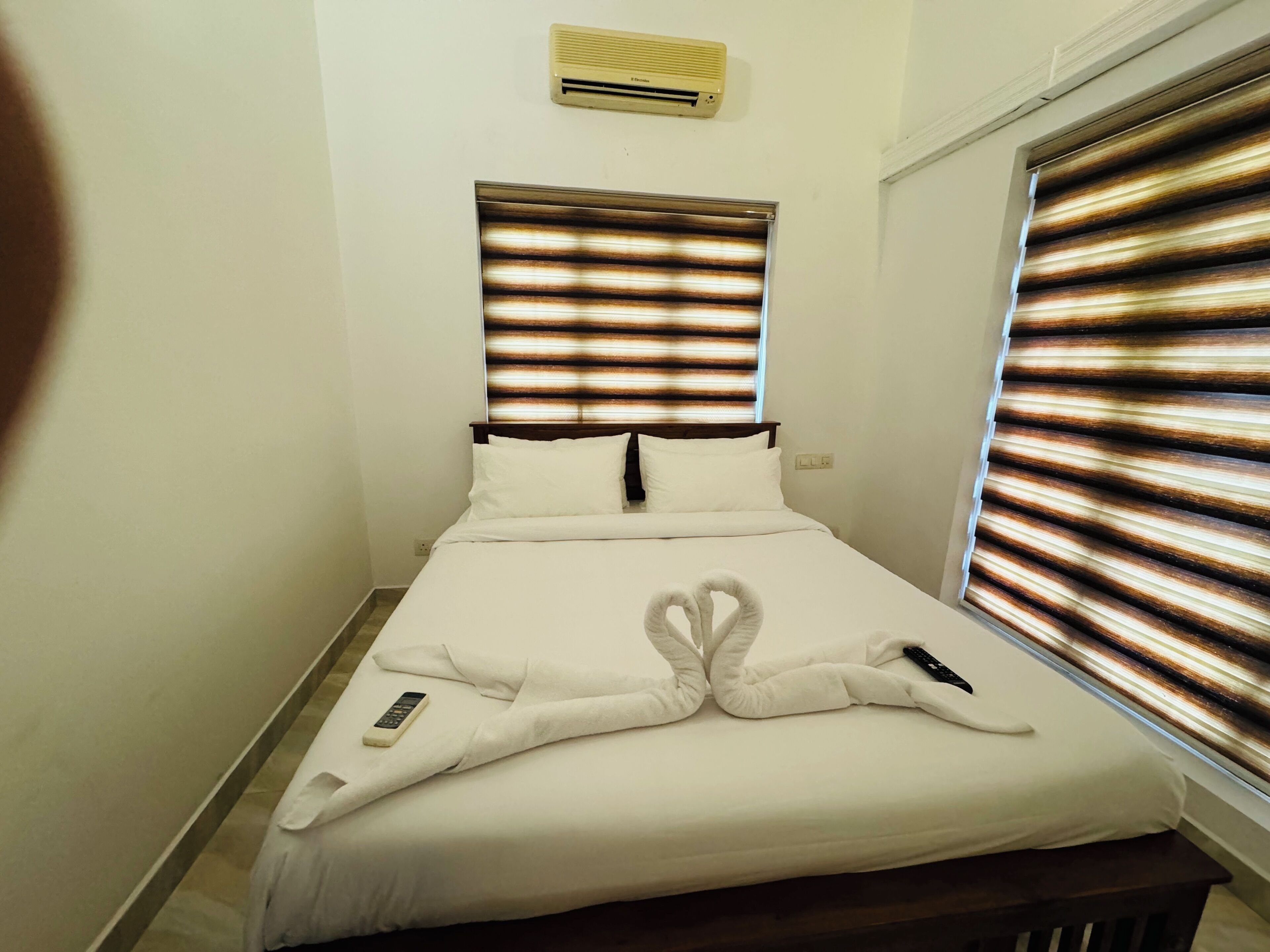 Een net opgemaakt bed met witte lakens, een afstandsbediening en een handdoek gevouwen in de vorm van een hart.