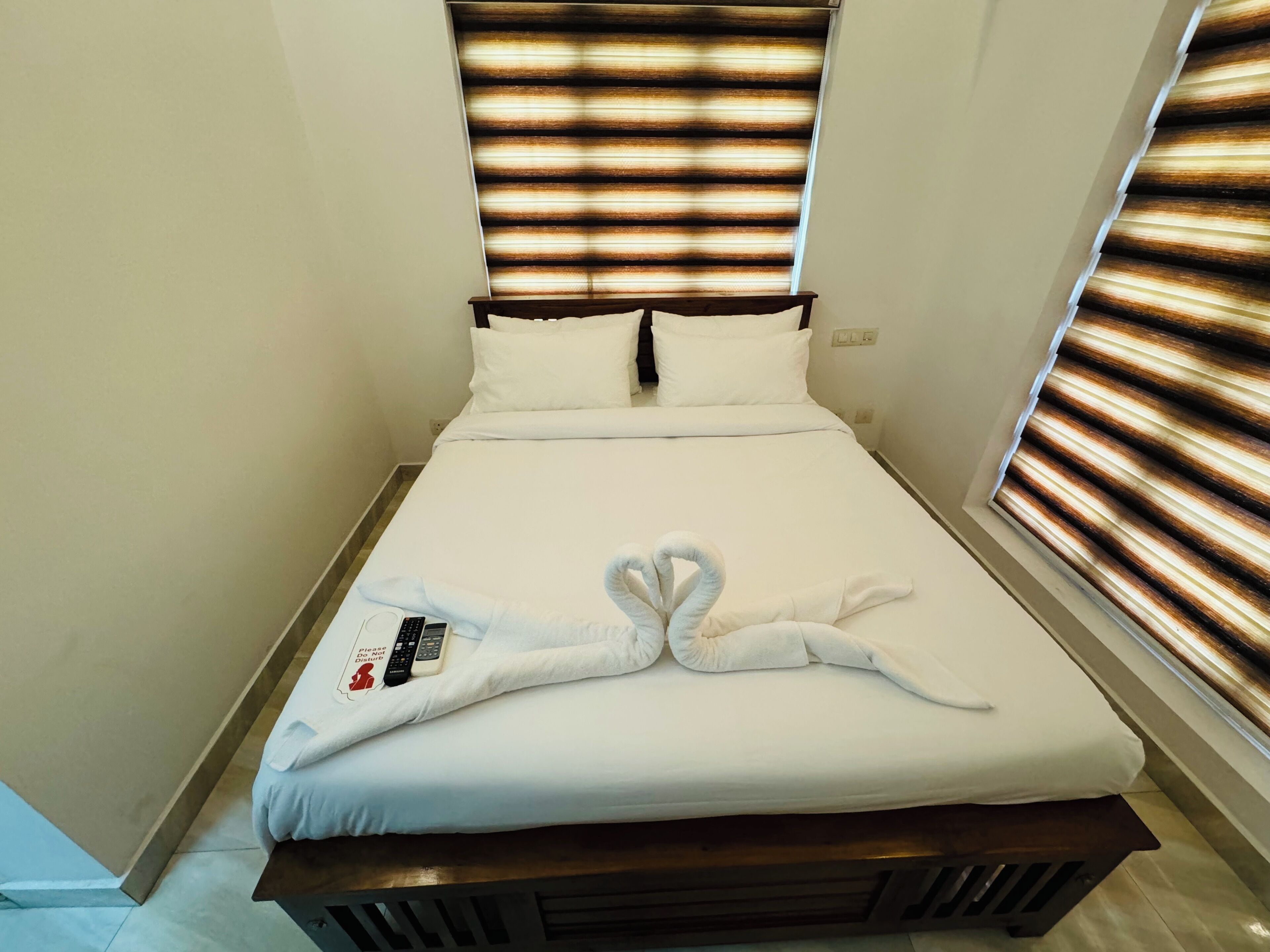A hotel room with a bed, white bedding, a towel artfully arranged on the bed, and a sign instructing to "Please do not disturb."