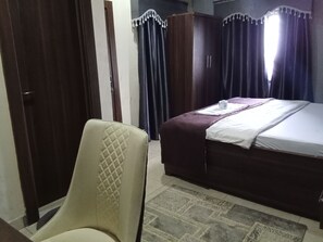 A hotel room with a bed, a chair, a wardrobe, and curtains.