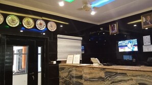 A reception area with a marble counter, clocks displaying time from various cities, a ceiling fan, and a television screen. - Dutse Suites and Luxury (Abuja)