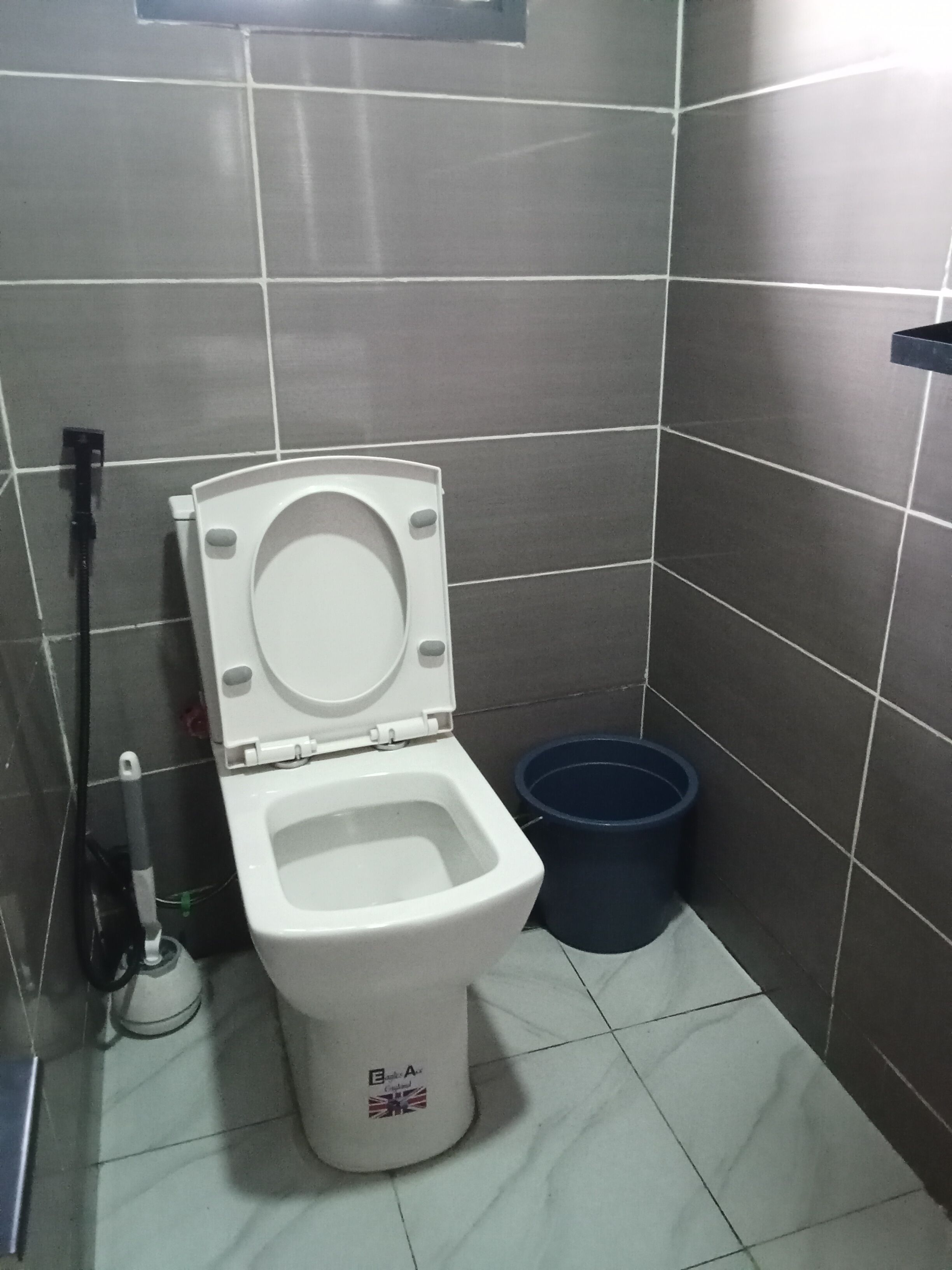 A small, compact bathroom with a white toilet, a blue trash bin, and a wall-mounted faucet.