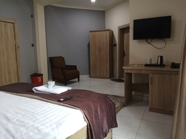 A hotel room with a bed, a chair, a desk, a television, and a wardrobe.