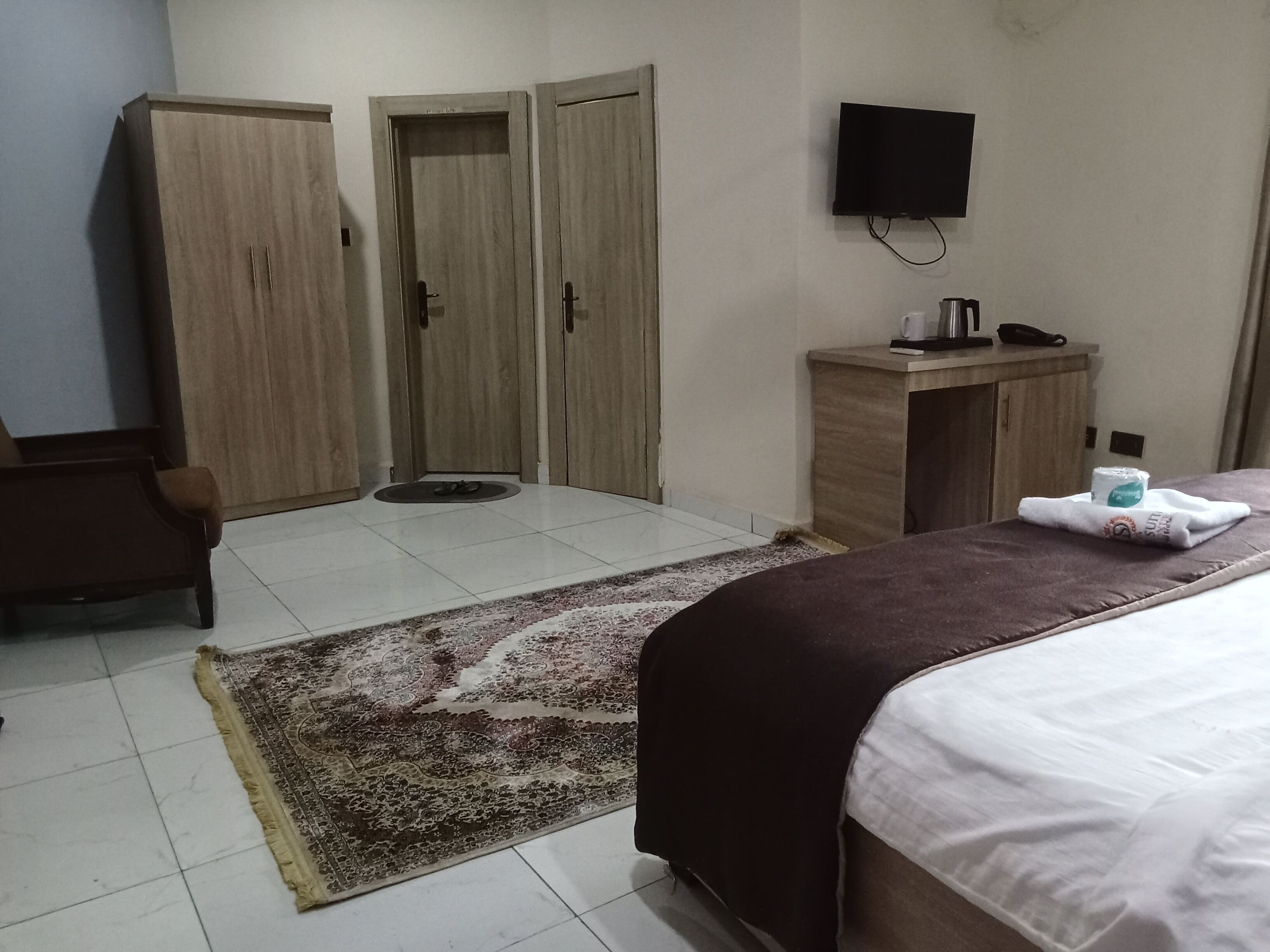 A hotel room with a bed, a desk, a chair, a TV, and a wardrobe.
