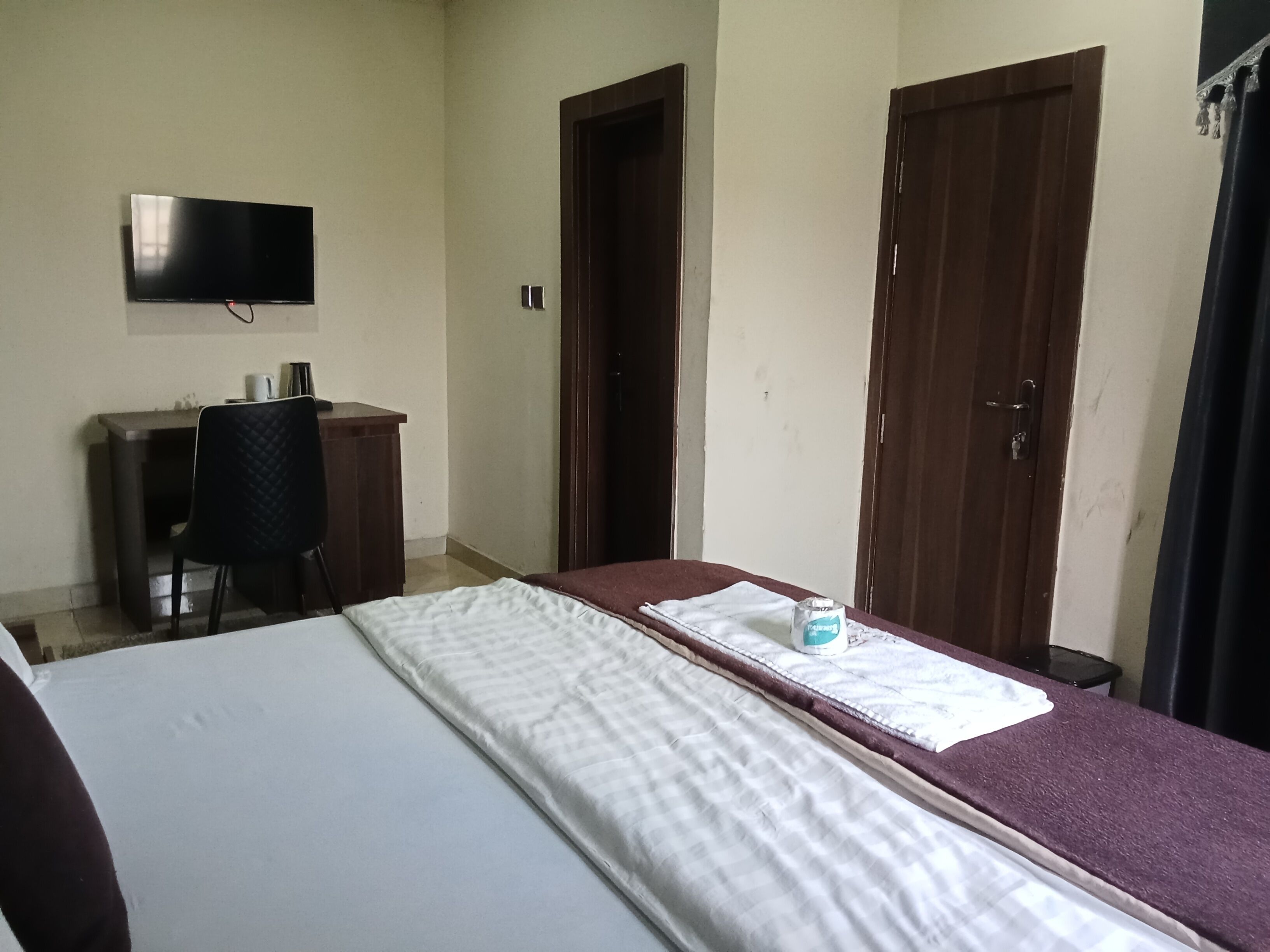 A room with a bed, a desk, a chair, and a television on the wall.