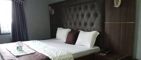 A neatly made bed with a dark headboard, a bedside table with a lamp, and a window with curtains.