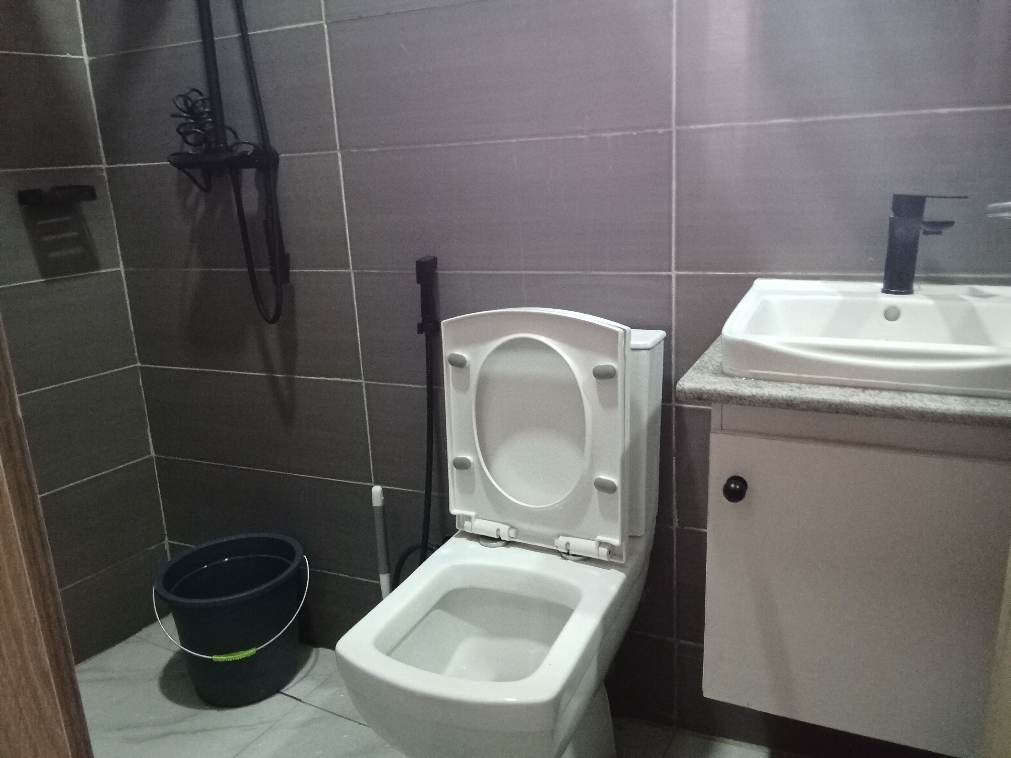 A bathroom with a toilet, a sink, and a black bucket.