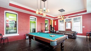 Ein Billardraum mit Pooltisch, einer Ledersofa und einer roten Backsteinwand.