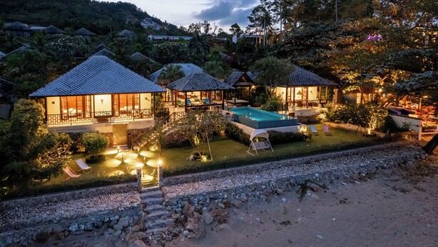 Een resort met meerdere bungalowgebouwen, een zwembad en een fraai onderhouden tuin.