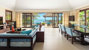 Een ruime woonkamer met een grote bank, een eettafel en stoelen. Via grote ramen is er uitzicht op de oceaan.