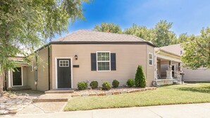 Une maison de plain-pied avec une porte d’entrée sombre, un petit porche et une pelouse bien entretenue.