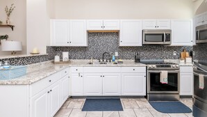 Une cuisine moderne avec des meubles blancs, un pare-feu noir et blanc, des appareils en acier inoxydable et un tapis bleu.