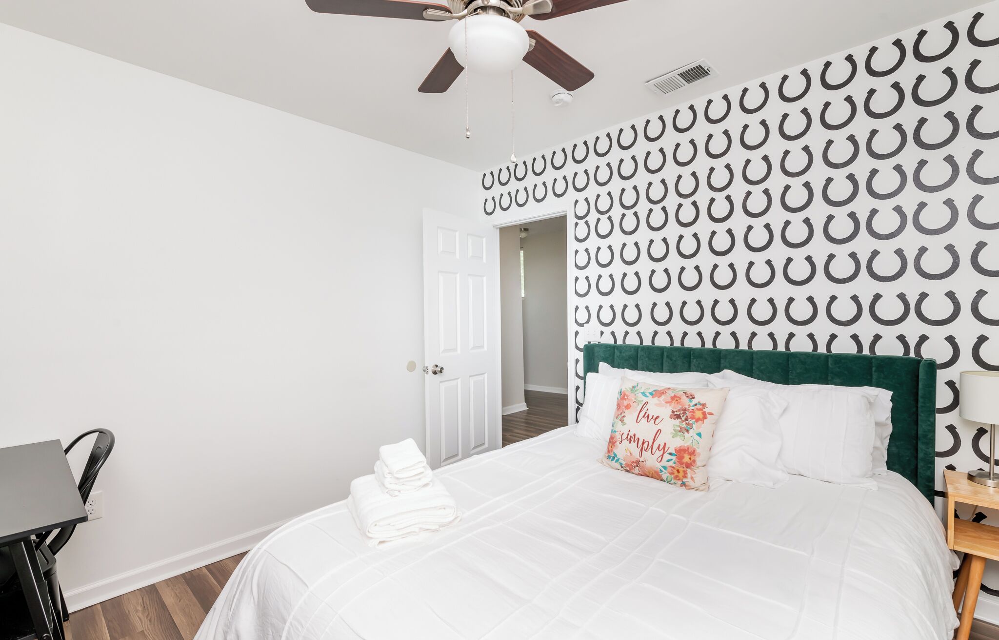 A bedroom with a bed, a desk, a chair, a ceiling fan, and a door.