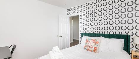 A bedroom with a bed, a desk, a chair, a ceiling fan, and a door.