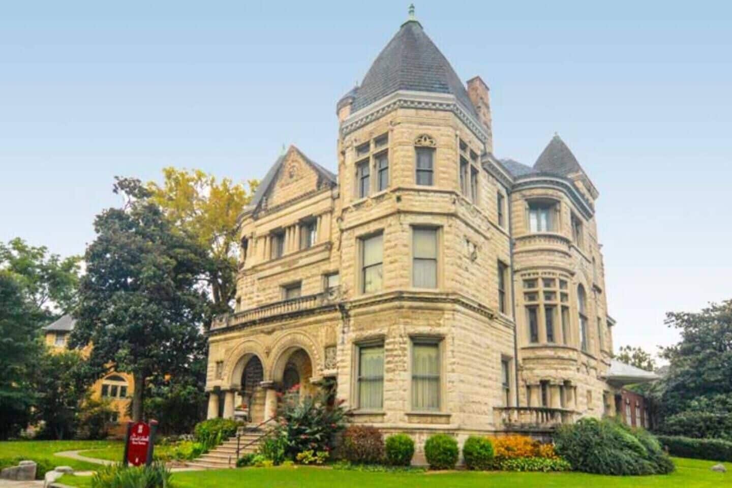 A large, historic stone building with multiple towers and arched windows, surrounded by well-maintained gardens.