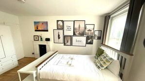 A bedroom with a bed, bedside tables, a bench, and a wall with framed pictures. - Charming studio apartment in Central London W2 (London)