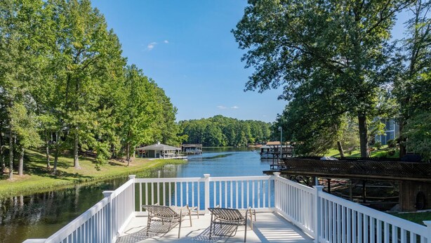 A deck with white railings overlooking a lake, surrounded by trees and a dock extending into the water. - New! Lakefront, Great Location, Pet Friendly (Henrico)