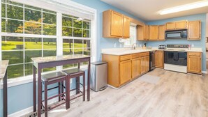 A kitchen with wooden cabinets, a stainless steel refrigerator, and a large window overlooking a green lawn. - New! Lakefront, Great Location, Pet Friendly (Henrico)