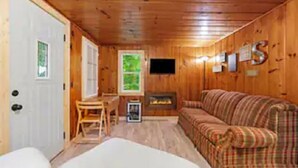 A log cabin interior with a plaid sofa, a fireplace, a television, and a small table with chairs.