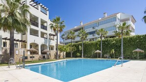A swimming pool with a clear blue water, surrounded by a paved area with palm trees and a building with balconies in the background. - Nice Seaview 2 Bed 2 Bath Apartm. (Benalmádena)