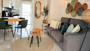 Una sala moderna con un sofá gris, una mesa redonda de madera y sillas verdes.