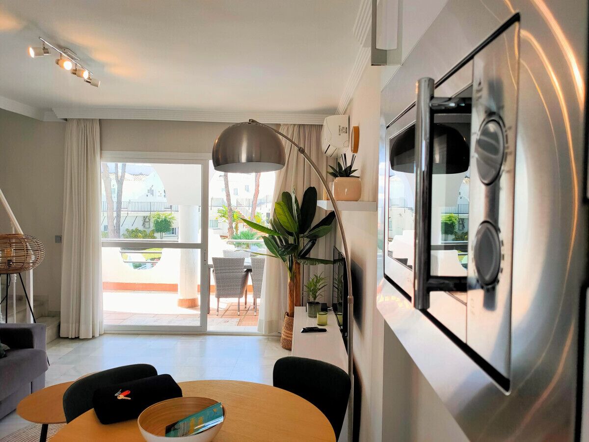 A modern kitchen with a stainless steel refrigerator, a dining area with a round table and chairs, and a large window offering a view of the outdoors.