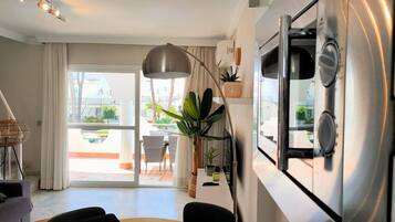 A modern kitchen with a stainless steel refrigerator, a dining area with a round table and chairs, and a large window offering a view of the outdoors.