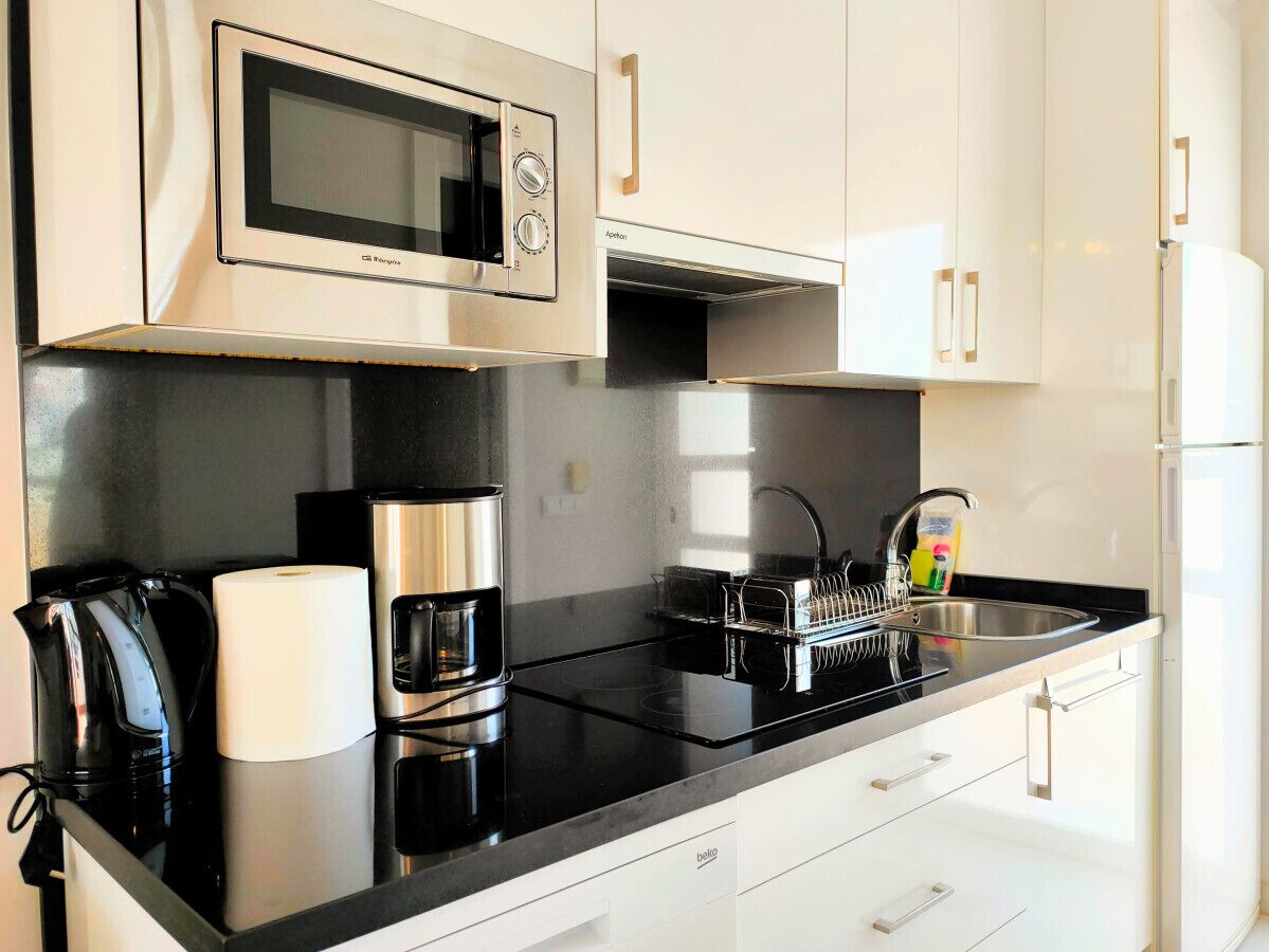 A modern kitchen with a microwave, coffee maker, kettle, and a sink with dish drying rack.