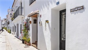 A narrow street lined with white buildings, each with a black door and a small balcony. A sign reading 'CASA RIJA' is visible on one building. - Casa Rija Mijas village by Casa del sol (Mijas)