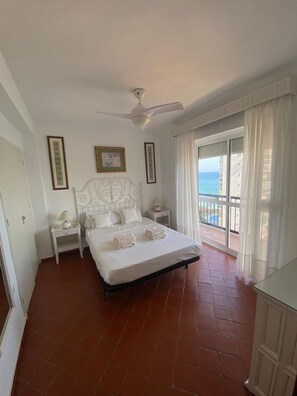 A bedroom with a bed, a nightstand, a ceiling fan, and a view of the sea through a balcony. - Casa Mily front Beach & pool (Mijas)