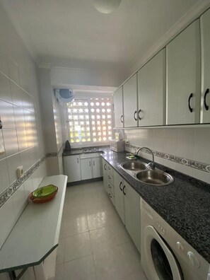 A kitchen with white cabinets, a sink, a washing machine, and a window with a view. - Casa Mily front Beach & pool (Mijas)