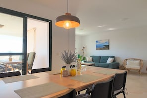 A modern living room with a dining area, a large window, and a painting on the wall.