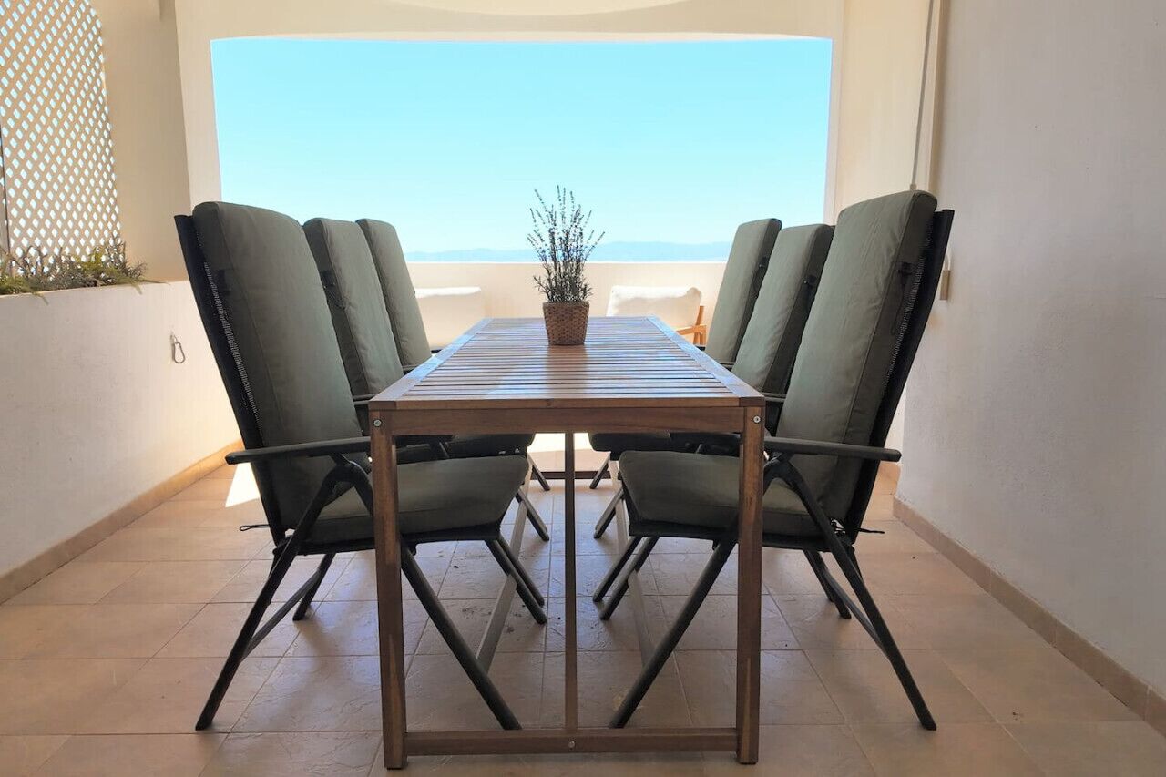 A dining table with four chairs, a potted plant, and a view of the sky.