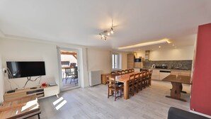 A modern living room with a wooden dining table and chairs, a flat-screen TV, and a sofa.