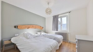 A bedroom with two beds, a wooden headboard, a radiator, a window with curtains, and a hanging light fixture.