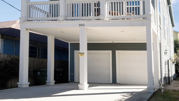 Un immeuble résidentiel à plusieurs étages, doté d’un balcon central, d’un garage et d’une petite structure en forme de tour sur le toit.