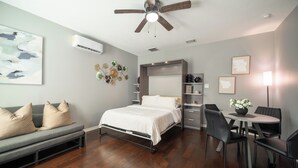 Une chambre moderne avec un lit, un canapé gris, une table à manger avec des chaises et un ventilateur de plafond.