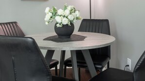 Un coin repas avec une table ronde, des chaises noires, un vase de fleurs blanches et des œuvres d’art encadrées accrochées au mur.